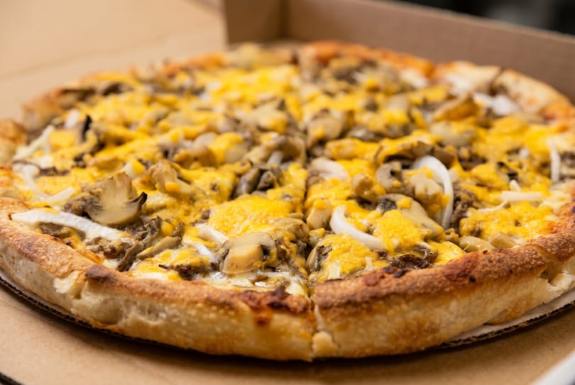 A whole pizza with mushrooms, onions, and melted yellow cheese in a cardboard box.