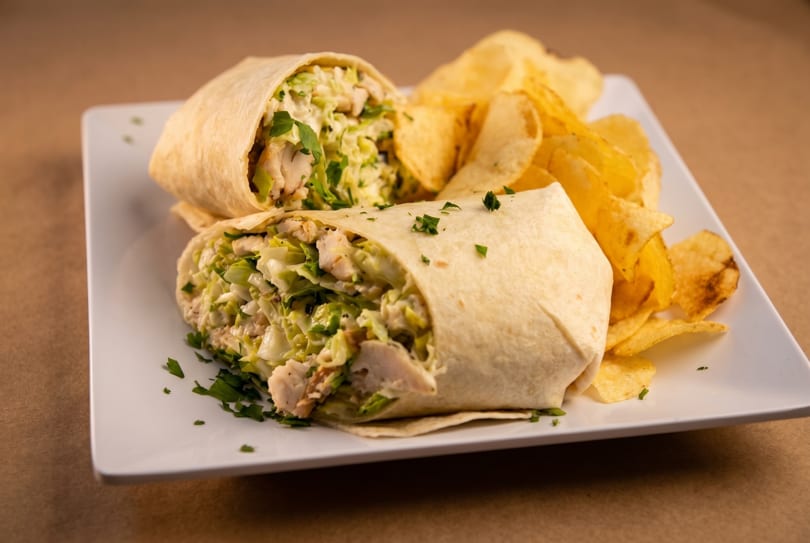 Two chicken wraps filled with lettuce and dressing, served with potato chips on a white plate.