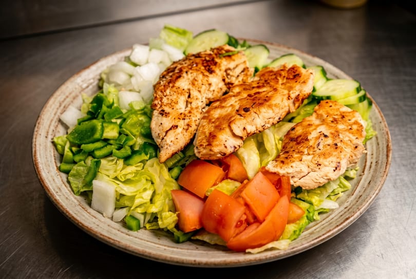 Grilled chicken breast slices on a bed of lettuce with chopped tomatoes, onions, green peppers, and cucumbers.