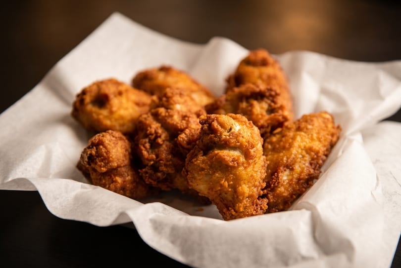 Crispy fried chicken pieces, golden brown, served in a white paper-lined basket.